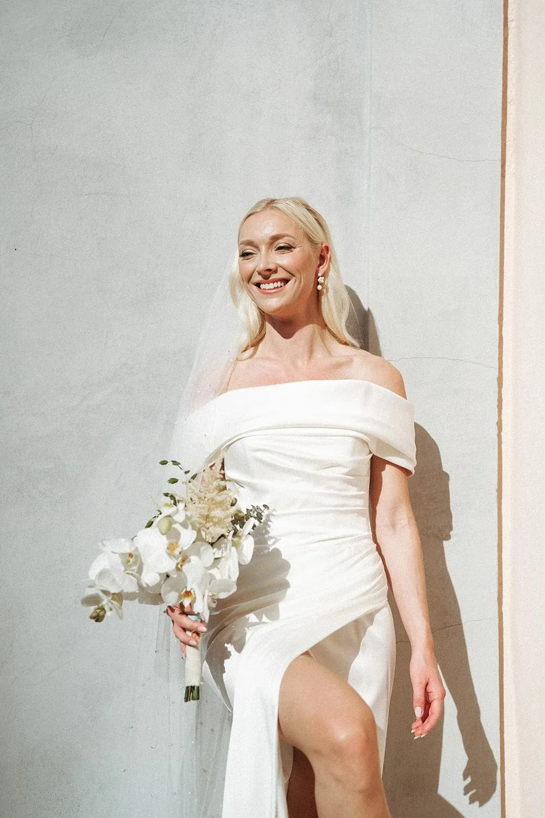 Alexandra leaning on a white wall, smiling